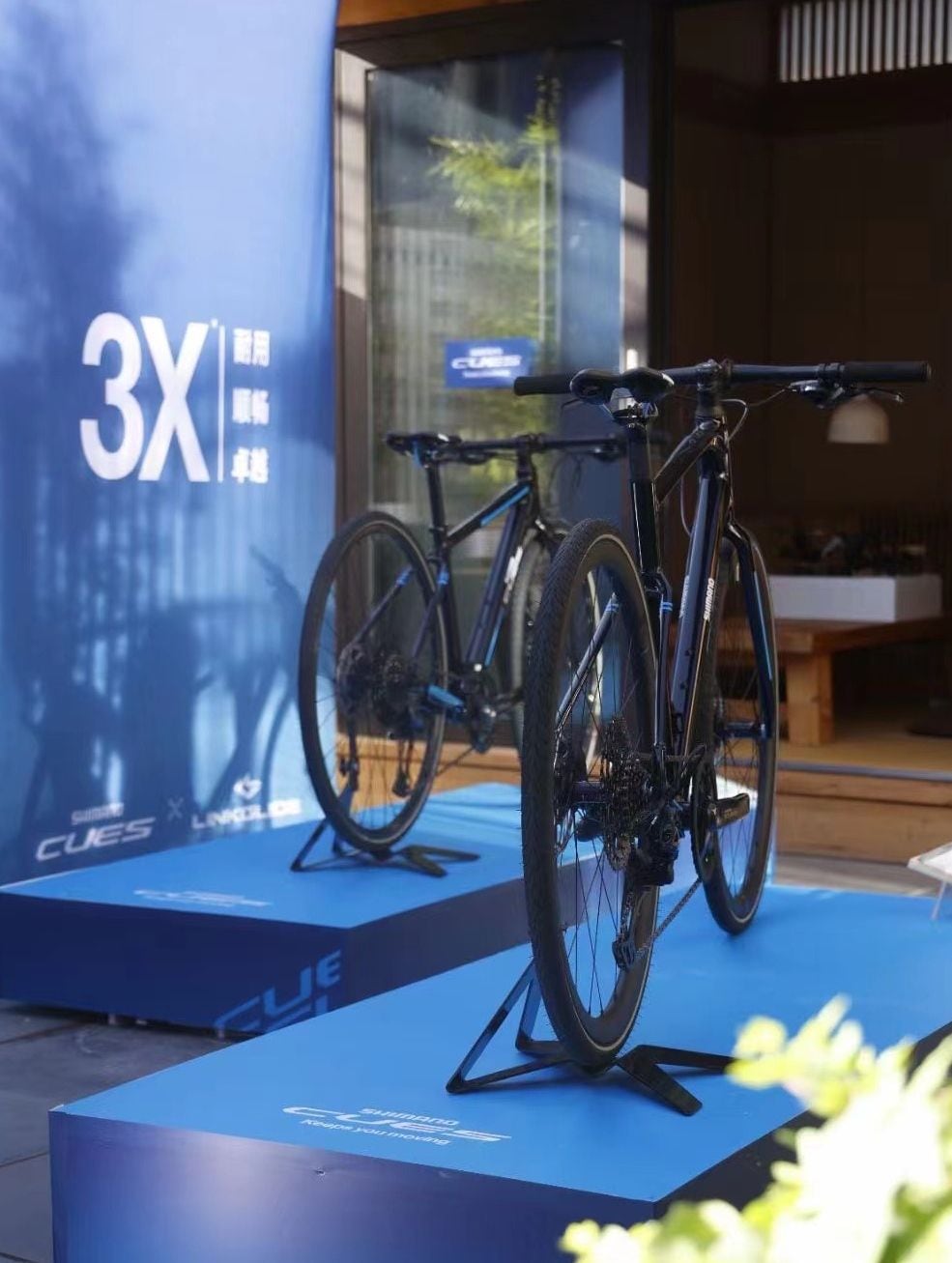 A bicycle on a stand in front of a blue backdrop with the text '3X' and 'CUE' visible.