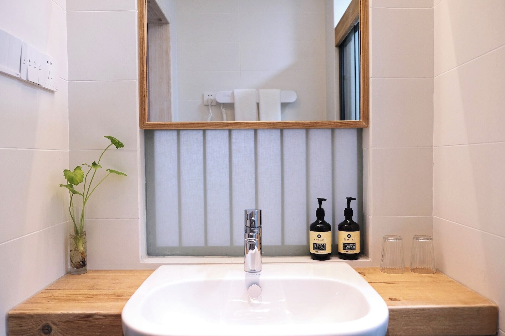 A bathroom with a white sink, a mirror, and two bottles of Apelles soap on the counter.