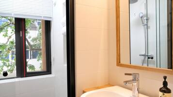 Un baño con ventana, lavabo, espejo y ducha.