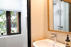 Un baño con ventana, lavabo, espejo y ducha.