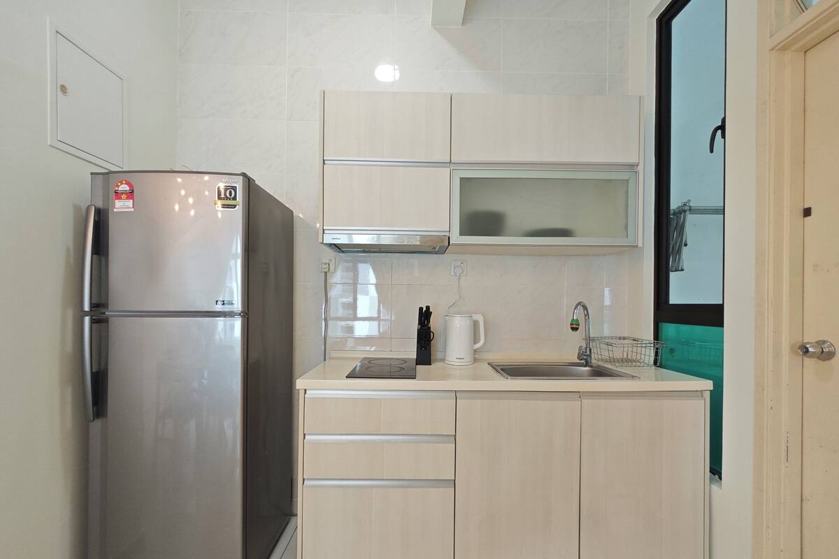 Een kleine keuken met een koelkast van roestvrij staal, een magnetron, een waterkoker en een spoelbak.