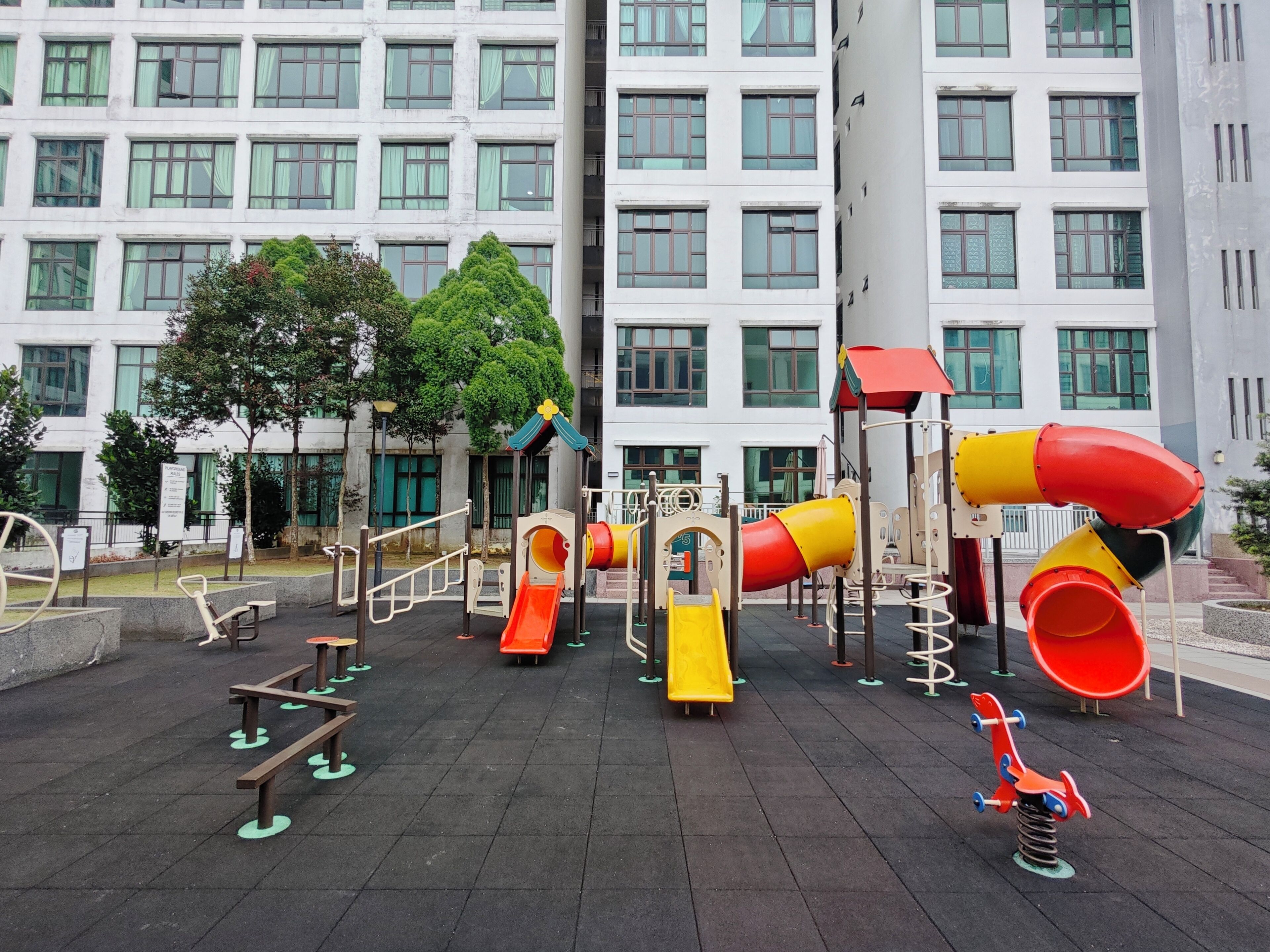 Un parque infantil con toboganes y estructuras de escalada, rodeado por un edificio con numerosas ventanas.