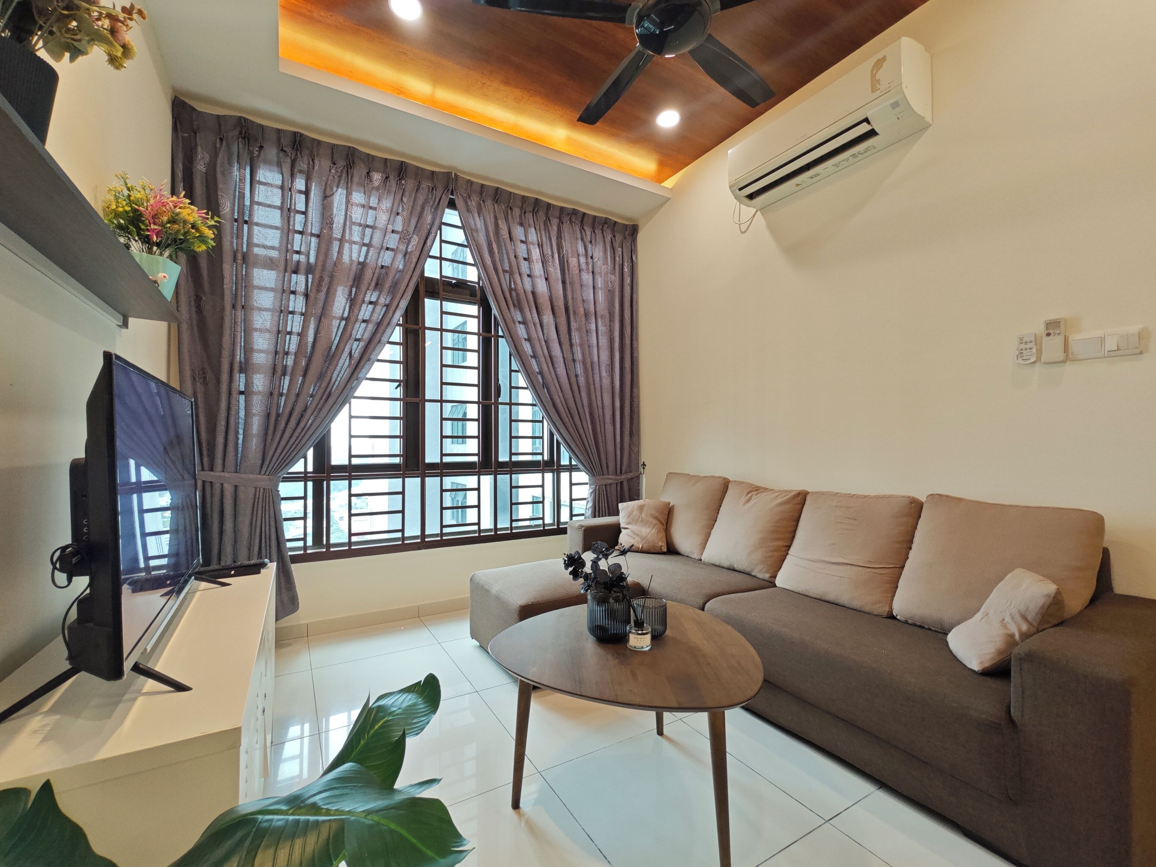A living room with a sofa, a coffee table, a TV, and a large window with curtains.