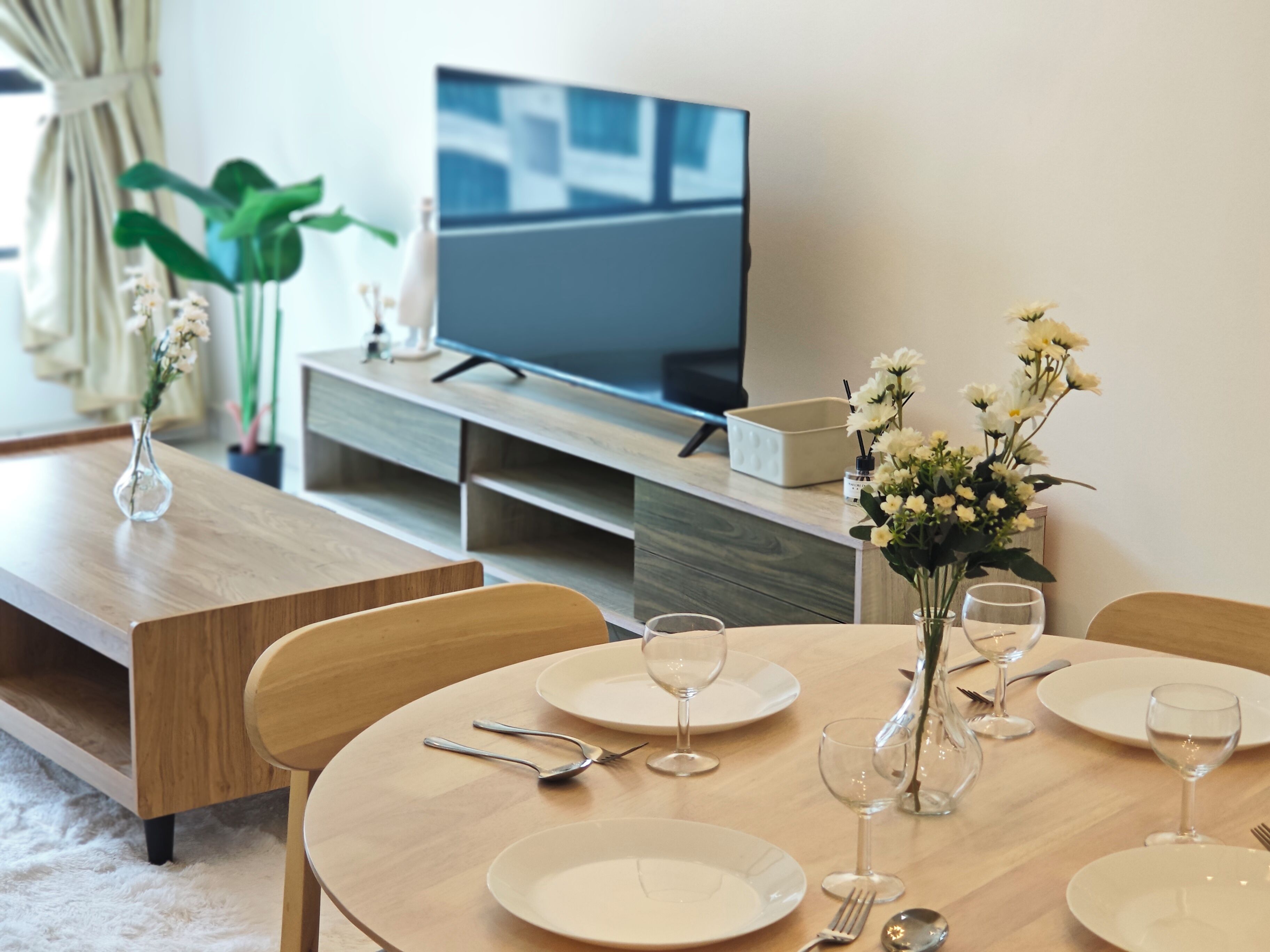 Ein Essbereich mit einem Holztisch, gedeckt für vier Personen, einem Fernseher auf einem Schrank und Topfpflanzen.