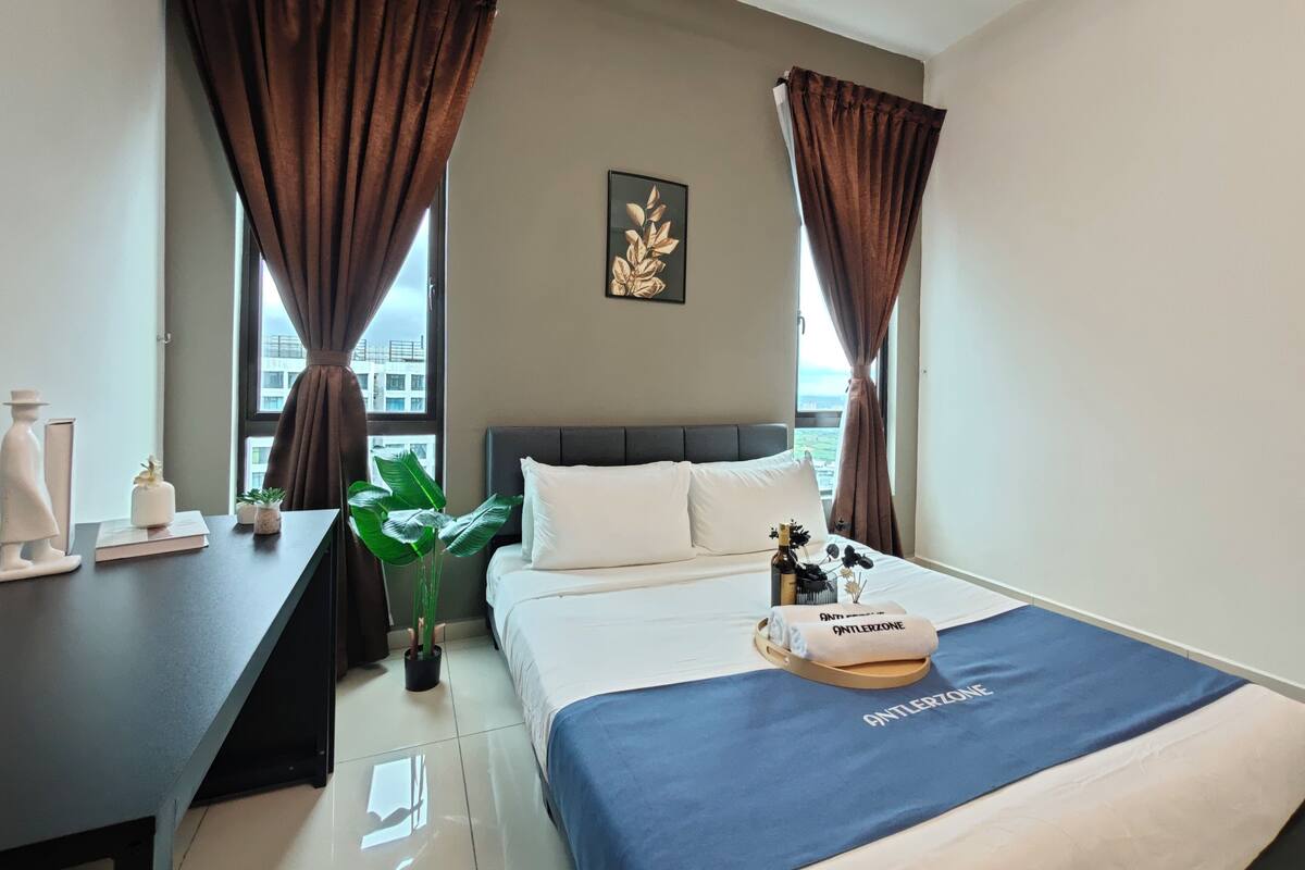 Een hotelkamer met een bed, een bureau, een potplant en uitzicht op gebouwen.