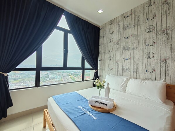 A hotel room with a large window, a bed with white bedding, a blue bedspread, and a decorative towel with the brand 'ANTLERZONE'. - Kempas Dsummit Residences by Antlerzone (Johor Bahru)
