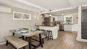 Una cocina moderna con armarios blancos, un refrigerador de acero inoxidable y un comedor con mesa y bancos de madera.