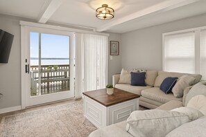 Een woonkamer met een bank, een salontafel, een deur naar een balkon en een plafondlamp.