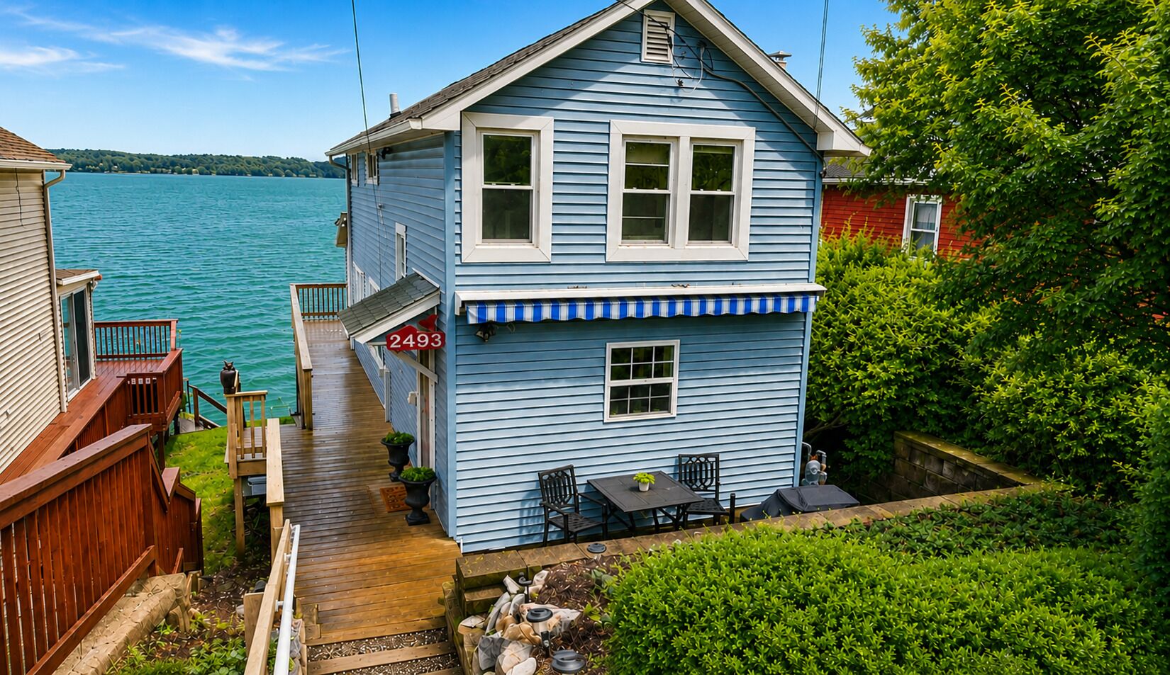 Une maison à deux étages avec un quai menant à un petit bateau, une plaque portant le numéro 2493 et une vue sur l’eau.