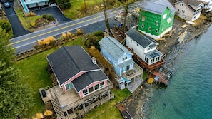 Vue aérienne d’une propriété située sur la côte, comprenant plusieurs maisons, un quai et une route.
