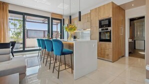 A modern kitchen with a central island, bar stools, and a view of the outdoors. - Starry Nights: Penthouse Sauna & Jacuzzi Serenade

 (Glifada)