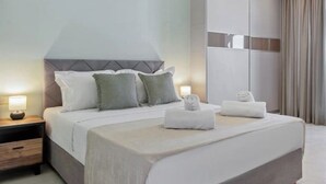A neatly made bed with pillows and a blanket, a bedside table with a lamp, and a large mirror on the wall. - Starry Nights: Penthouse Sauna & Jacuzzi Serenade

 (Glifada)