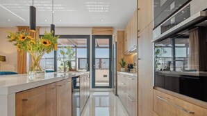 A modern kitchen with wooden cabinets, a central island, and a view to the outside. - Starry Nights: Penthouse Sauna & Jacuzzi Serenade

 (Glifada)
