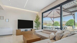 A modern living room with a large flat-screen TV, a wooden coffee table, and a beige sofa. - Starry Nights: Penthouse Sauna & Jacuzzi Serenade

 (Glifada)