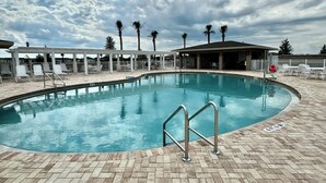 Una piscina con solárium de ladrillo, sillas de descanso y palmeras al fondo.