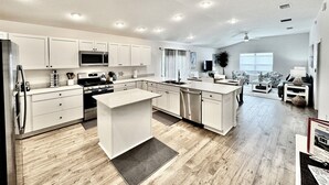 Una cocina moderna con armarios blancos, una isla central y una zona de comedor con sofá y mesa de centro.