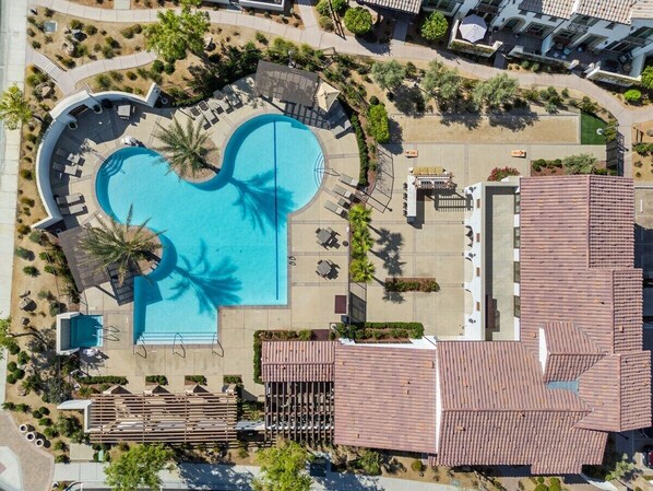 An aerial view of a resort with a large swimming pool, lounge areas, and a building with a tiled roof.