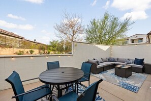 An outdoor patio with a round table and chairs, a sofa with cushions, and a decorative rug.