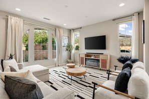 A modern living room with a sofa, round coffee table, and a flat-screen TV mounted on the wall. - Golfers' Retreat: Near PGA West & Luxury Pool (La Quinta)