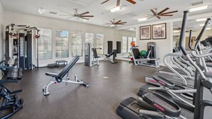 Une salle de sport équipée de ventilateurs de plafond, de tapis de course et d’appareils d’exercice.