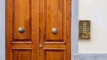 Una coppia di porte in legno con una basetta in ottone, un cancello decorativo in ferro battuto sopra e una targa con il numero '16' sulla parete.