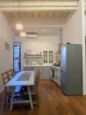 A kitchen with a dining table, chairs, a refrigerator, and a window.