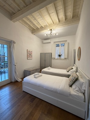 A bedroom with two beds, a window with curtains, a radiator, and a wooden ceiling.