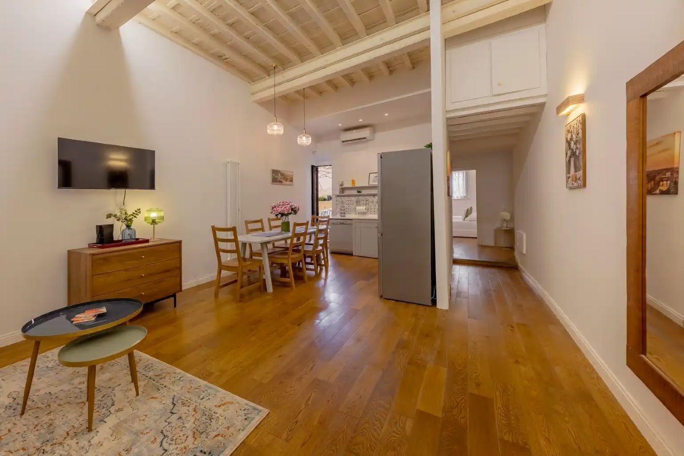 Un'ampia zona giorno con tavolo da pranzo, sedie, divano, televisione e cucina sullo sfondo.