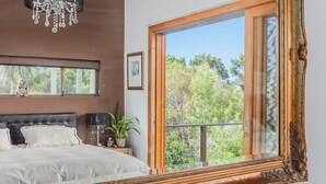 Un dormitorio con una cama grande, un candelabro, una ventana con marco de madera y un balcón con árboles.
