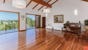 Una habitación amplia con suelo de madera, ventanas grandes y un balcón con vistas a zonas verdes.