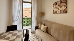 A room with a sofa, a table with a checkered tablecloth, a lamp, and a window with curtains. - Green Heart House Napoli (Naples)