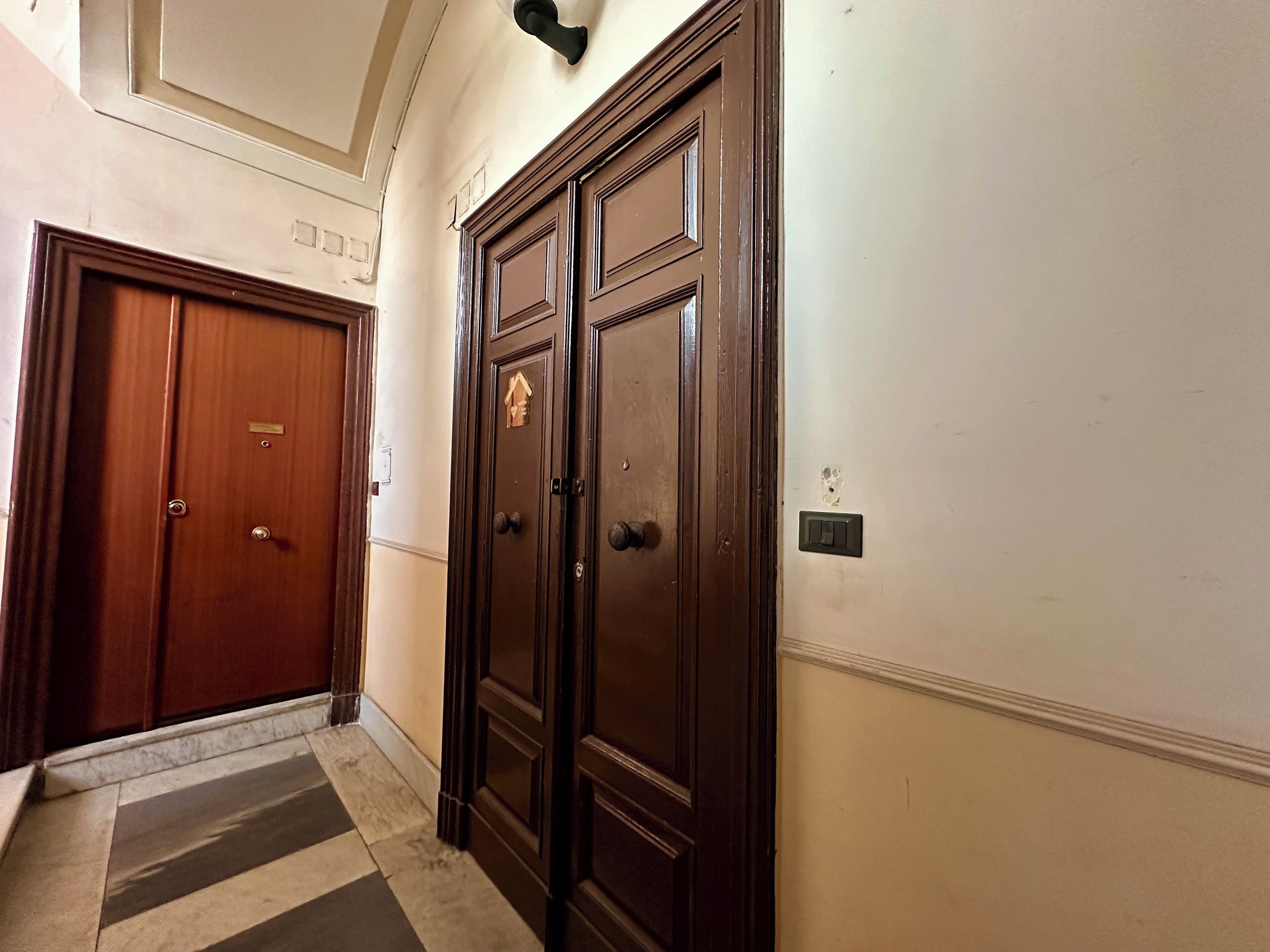 A hallway with a wooden door and a wall-mounted light fixture.