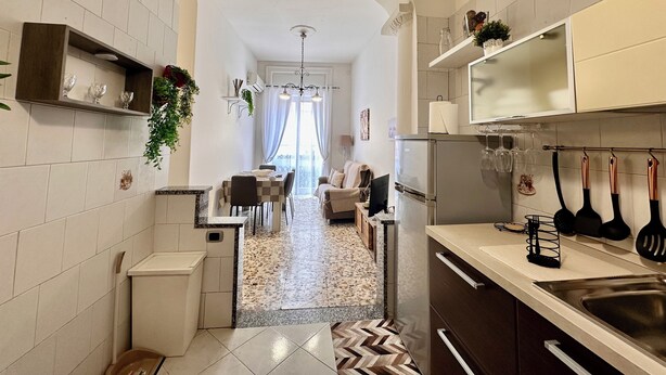 A narrow kitchen with a dining area in the background, a refrigerator, and various kitchen utensils. - Green Heart House Napoli (Naples)