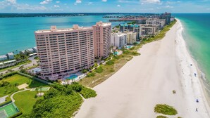 Un hotel frente al mar con varios edificios altos, una playa de arena y un cielo azul despejado.