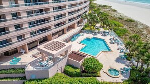 Un hotel con zona de piscina, sillones de descanso y vista a la playa.