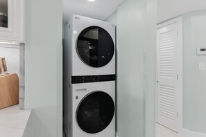A wall-mounted laundry unit with two cylindrical compartments, a white door with horizontal louvered panels, and a digital thermostat on the wall. - 🌞CBC 2-10C - Beachfront-Pool-Hot Tub-Gym-Tennis!🏖️ (Clearwater Beach)