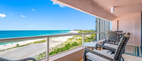Ein Balkon mit Korbmöbeln, Blick auf den Strand und eine Stadtlandschaft im Hintergrund.