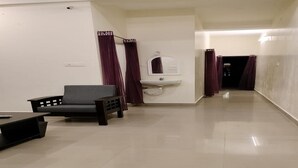A spacious, well-lit hallway with a grey sofa, a white sink, and purple curtains. - Gokulam Villa (Puducherry)