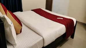 A single bed with a white mattress and a red blanket, a pillow with a red and beige design, and a wooden headboard. - Gokulam Villa (Puducherry)
