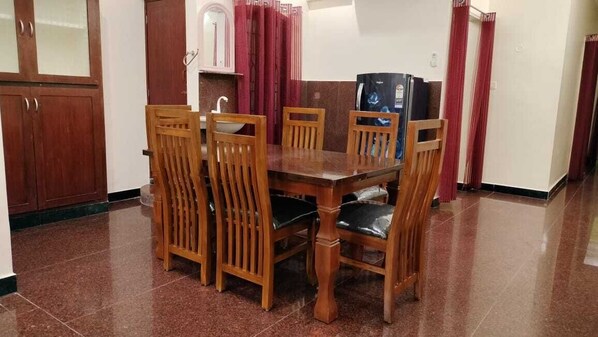 A dining area with a wooden table and chairs, a sink, and a refrigerator. - Gokulam Villa (Puducherry)