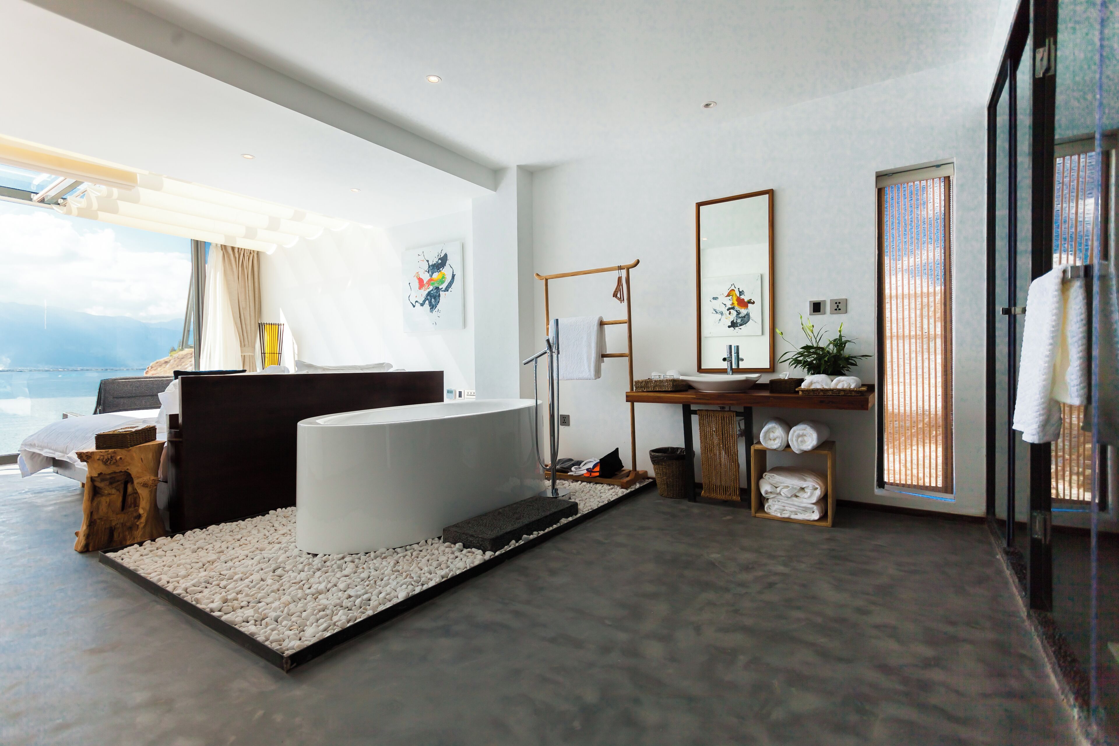 A modern bathroom with a bathtub, a vanity with a mirror, and a large window with a view of the outdoors.