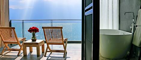 A balcony with two wooden chairs, a small table, and a vase of red flowers.