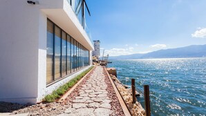 Un paseo marítimo con un camino de piedra que lleva a un edificio con amplias ventanas con vistas al agua.