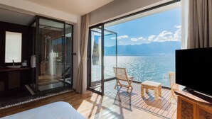Habitación de hotel moderna con un gran ventanal corredero que da a un balcón con vistas al mar y a las montañas.