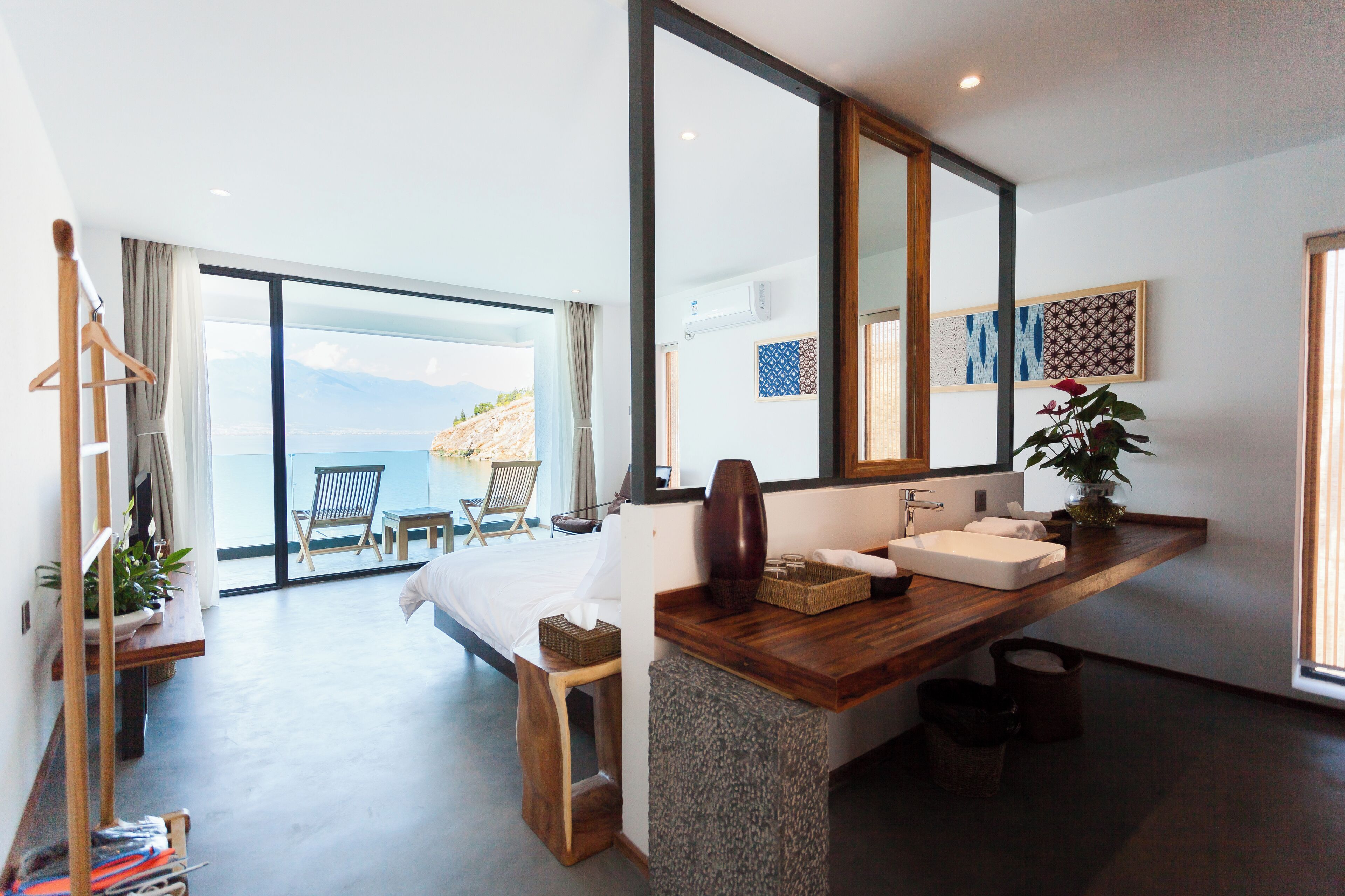 A modern hotel room with a large bed, a wooden vanity, a large mirror, and a view of the sea.