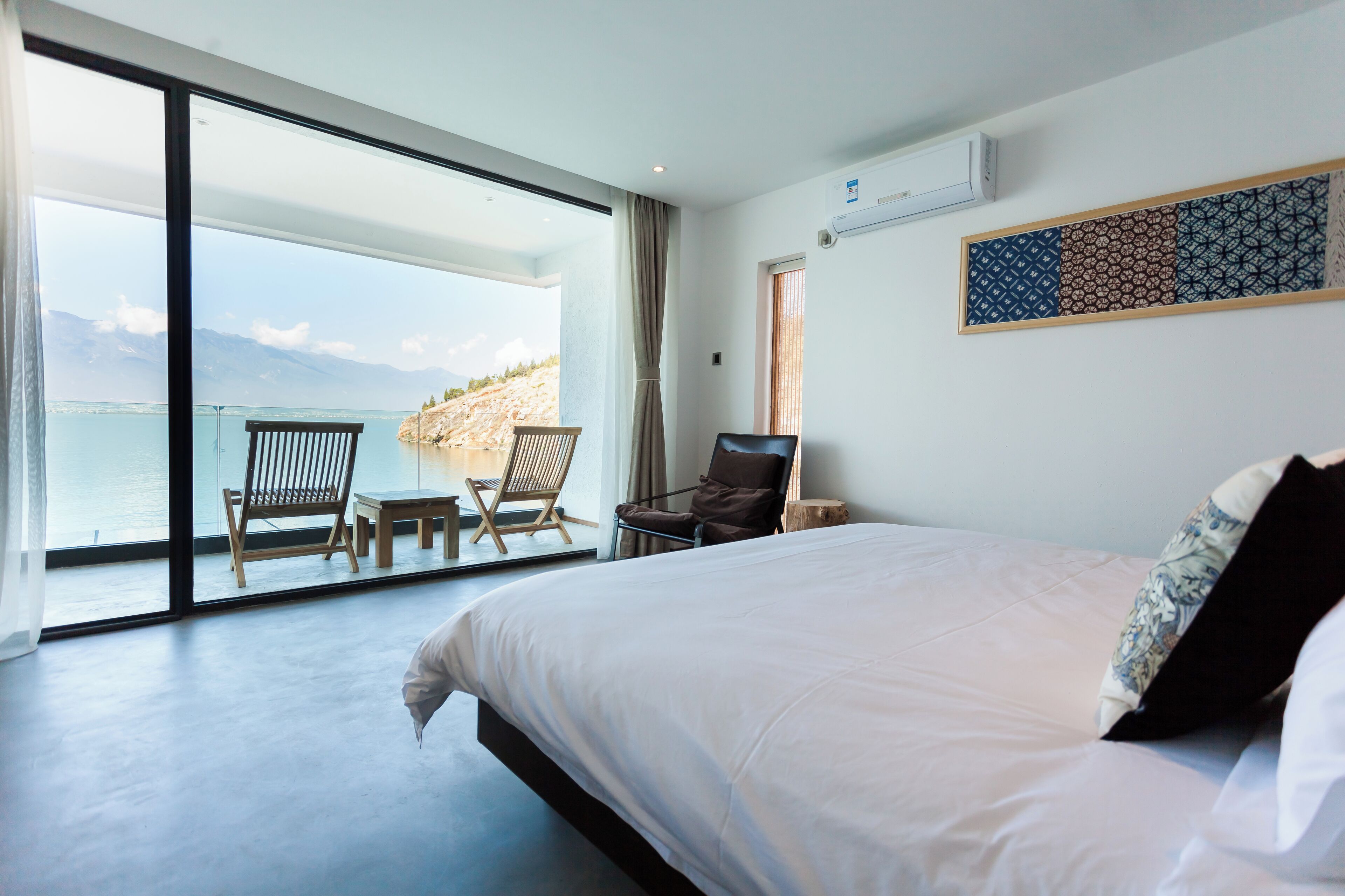 A bedroom with a large bed, a view of the sea, and a seating area with chairs.