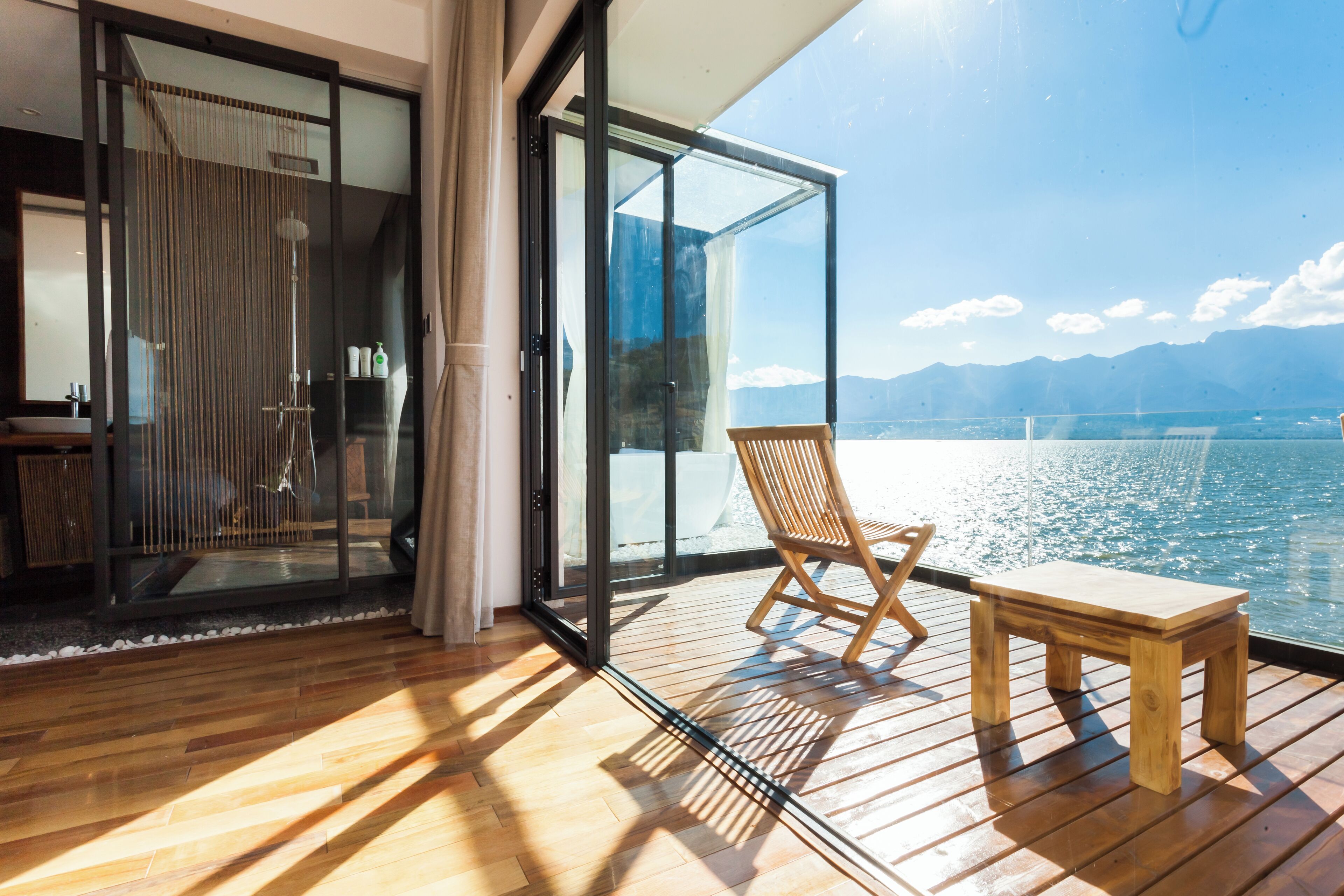 A wooden deck with a wooden bench and a glass door leading to a room.