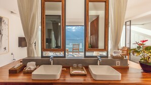 Un baño con un espejo grande, dos lavamanos y vistas al mar.