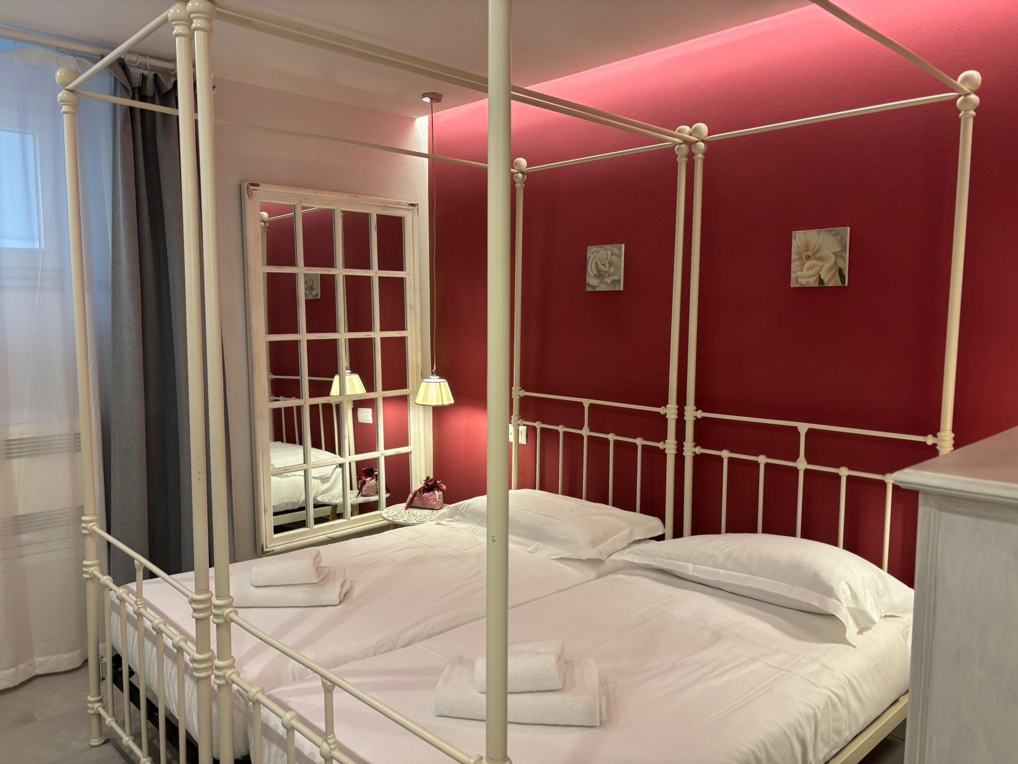 Ein Raum mit roten Wänden, ausgestattet mit einem Himmelbett, weißer Bettwäsche, einem Spiegel und zwei Wandleuchten.