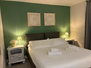 A neatly made bed with white linens, two wall-mounted lamps, and a small bedside table with a lamp and flowers.